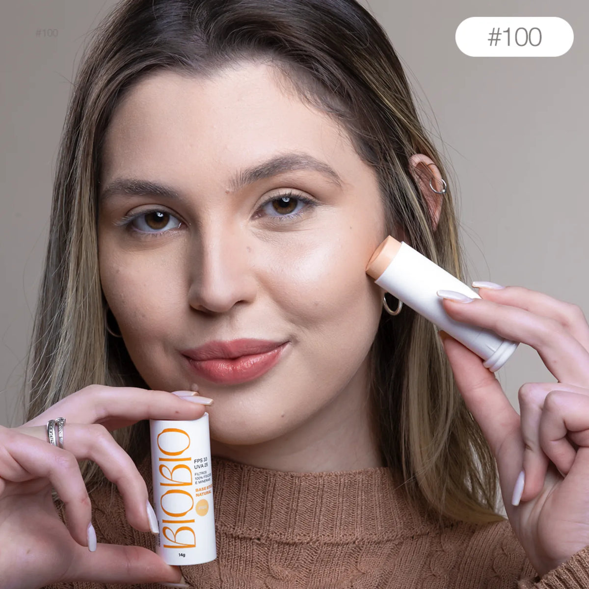 Base Multifuncional em Bastão BioBio tom Avelã #100 sendo aplicada diretamente no rosto de modelo com pele clara, demonstrando a praticidade da aplicação.
