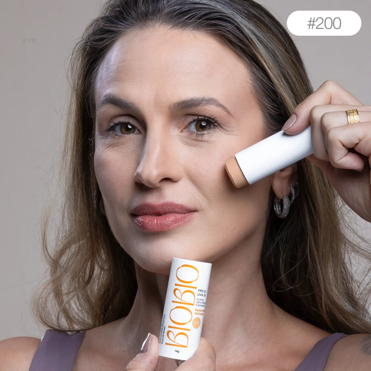 Base Multifuncional em Bastão BioBio tom Amêndoa #200 sendo aplicada diretamente no rosto de modelo madura com pele média, demonstrando a praticidade da aplicação.