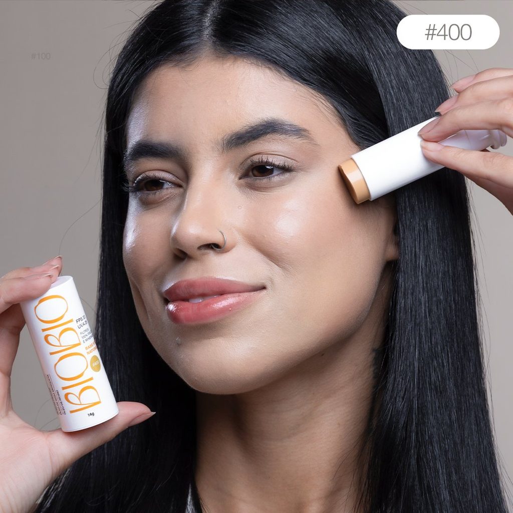 Base Multifuncional em Bastão BioBio tom Mascavo #400 sendo aplicada diretamente no rosto de modelo com pele média e cabelo liso escuro, demonstrando a praticidade da aplicação.