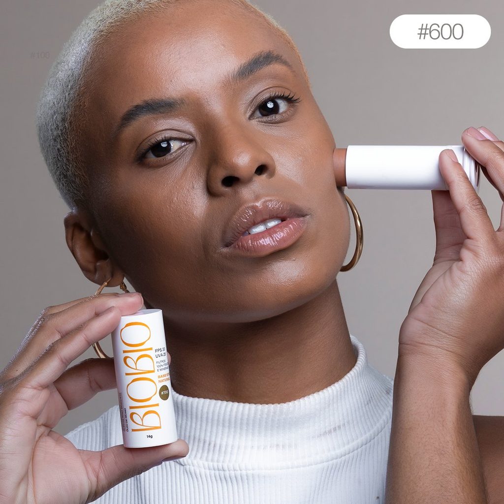 Base Multifuncional em Bastão BioBio tom Cacau #600 sendo aplicada no rosto de modelo com pele negra e cabelo curto, demonstrando a adaptação do produto a tons de pele mais escuros.