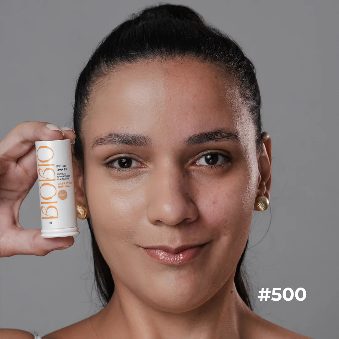 Base Multifuncional em Bastão FPS 33 da BioBio no tom #500 Canela: modelo segura o bastão de 14 g ao lado do rosto.