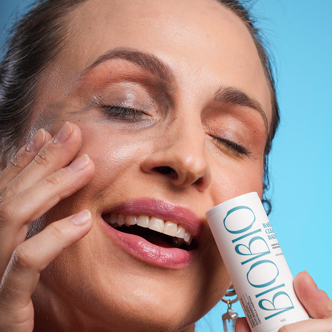 Demonstração de uso do Cleansing Balm em bastão BioBio. Mulher remove maquiagem escura dos olhos com o produto, evidenciando sua textura e poder de limpeza.